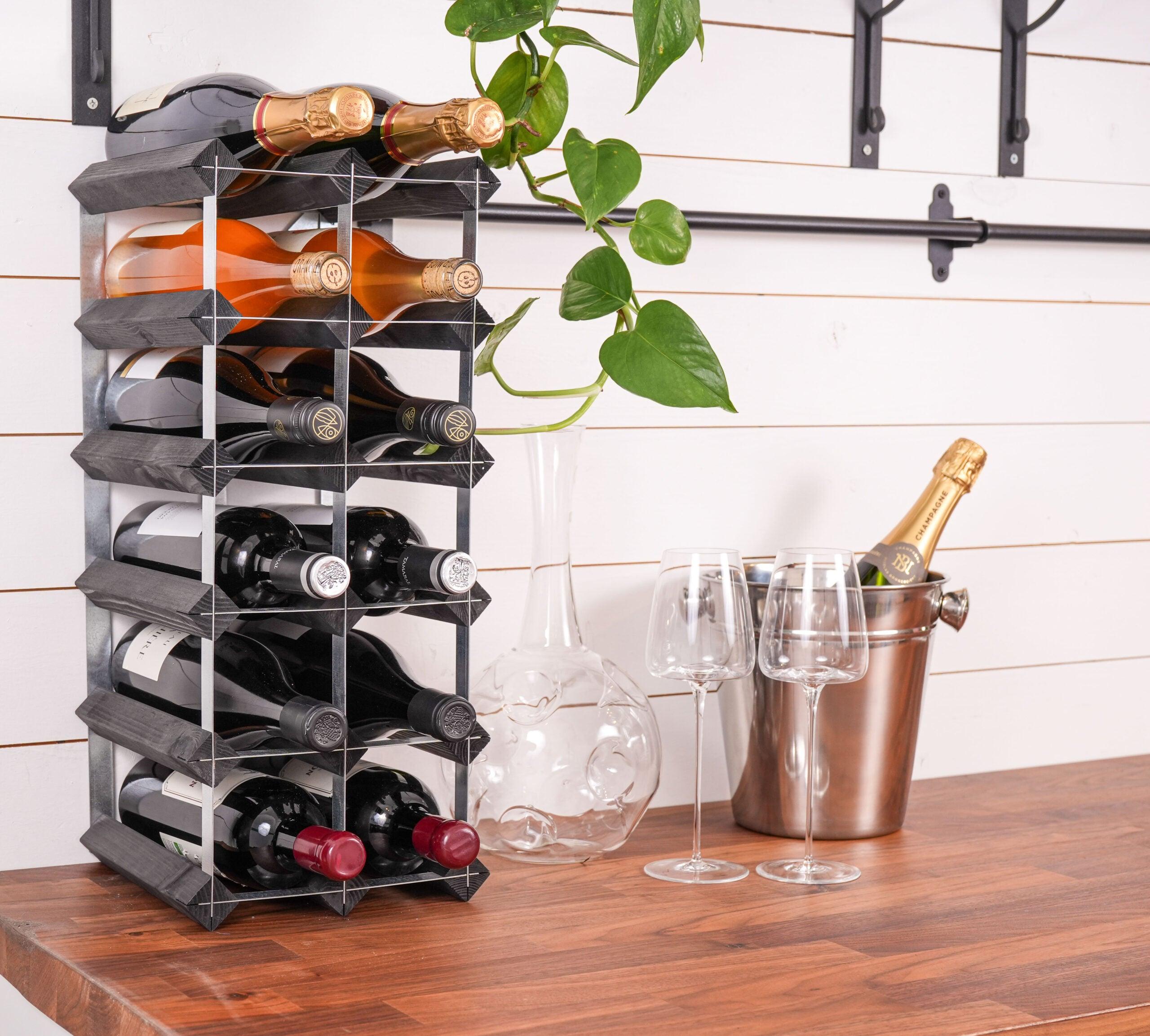 Vinreol som du selv skal samle i sort ask som står fyldt med vinflasker og vinglas og vinkaraffel ved side naf