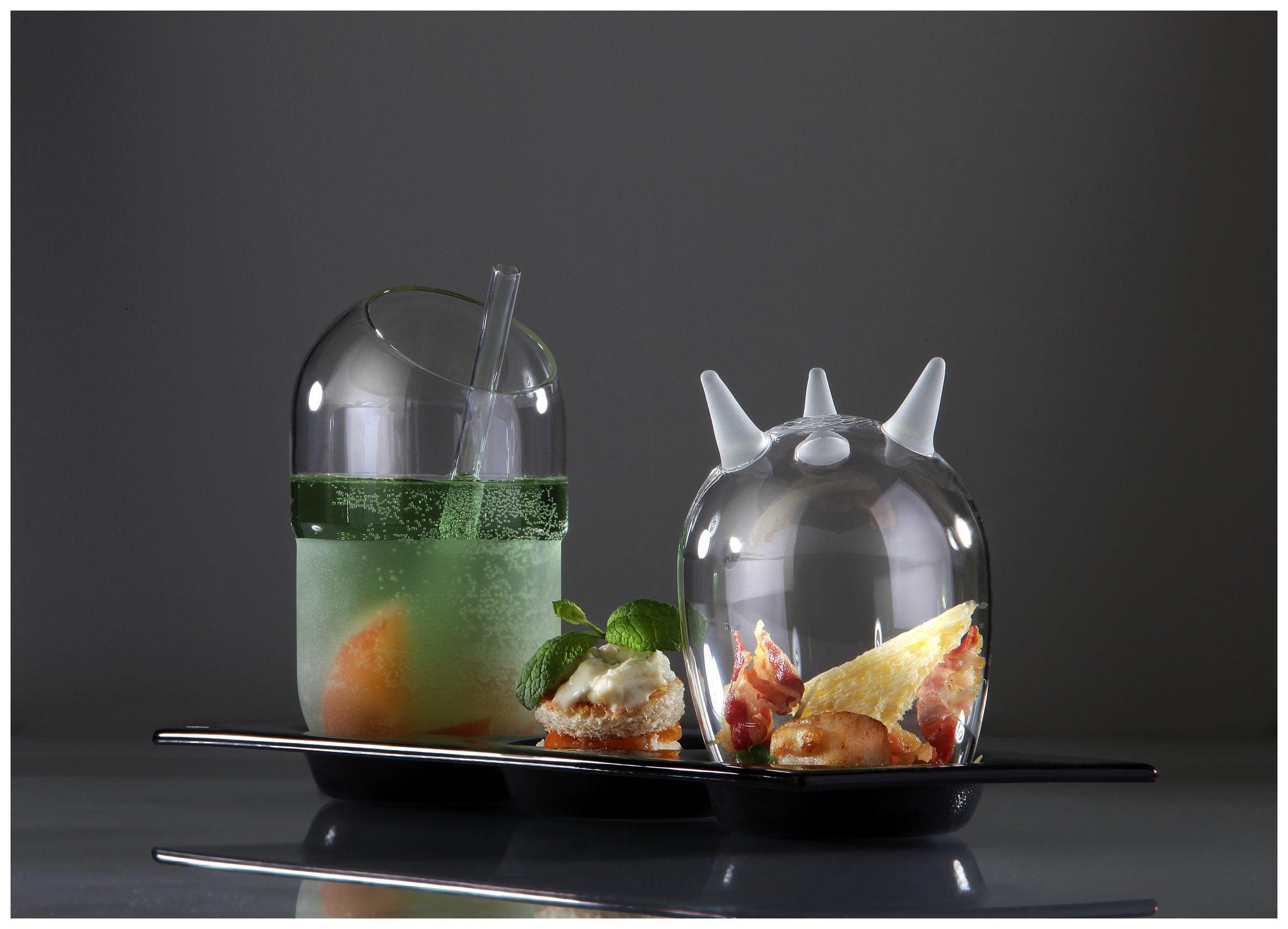 Elegant servering med La Rochere glas, hvor det ene glas indeholder en grøn drink med frugt og mynte, og det andet glas indeholder små appetitvækkere under en kuppel. Glasset står på en sort serveringsbakke, hvilket skaber en sofistikeret præsentation