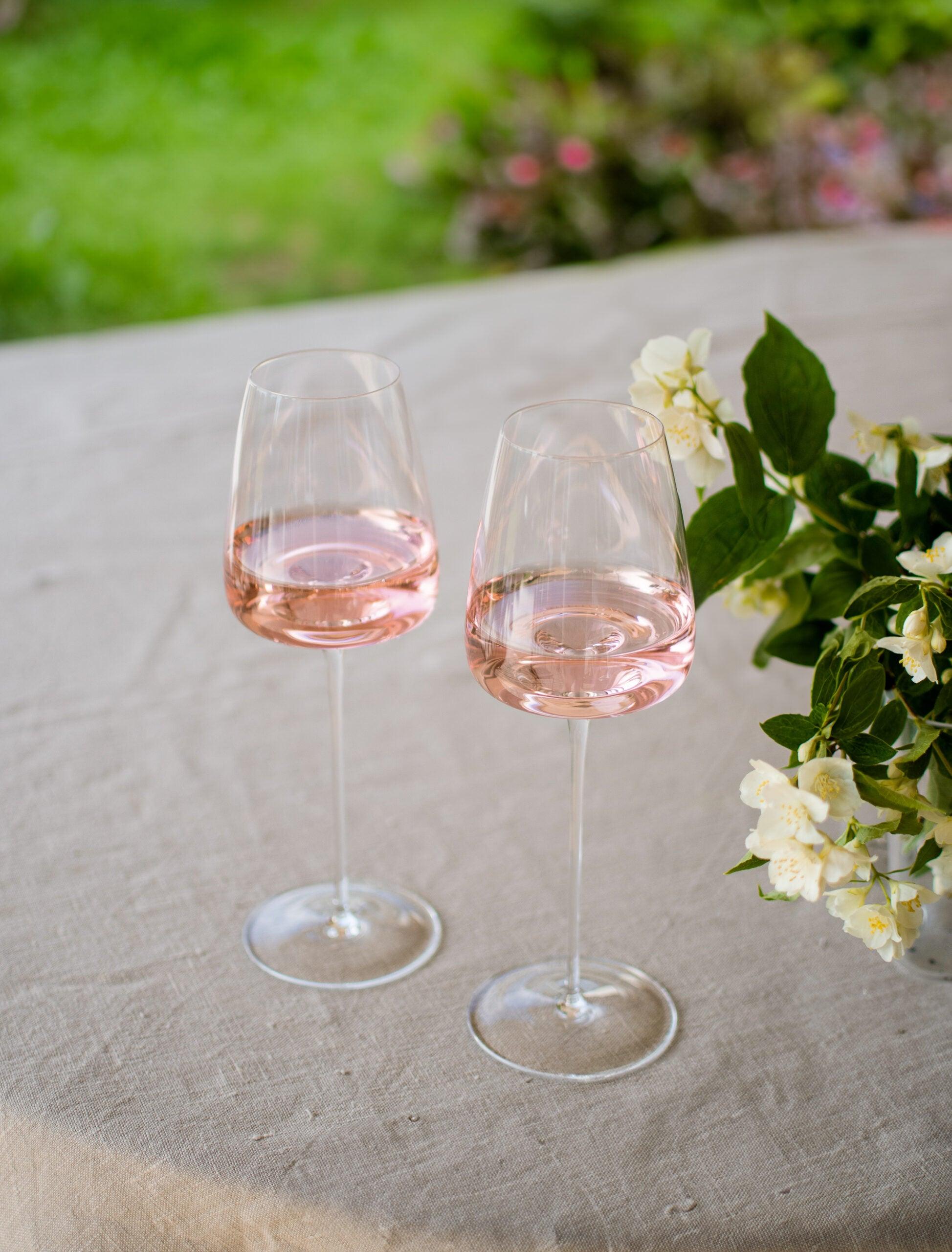 To Zieher Hvidvinsglas fra serien Vision Fresh står på et bord med hvid dug, fyldt med rosévin. Bordet er dekoreret med hvide blomster, og i baggrunden ses en grøn have.