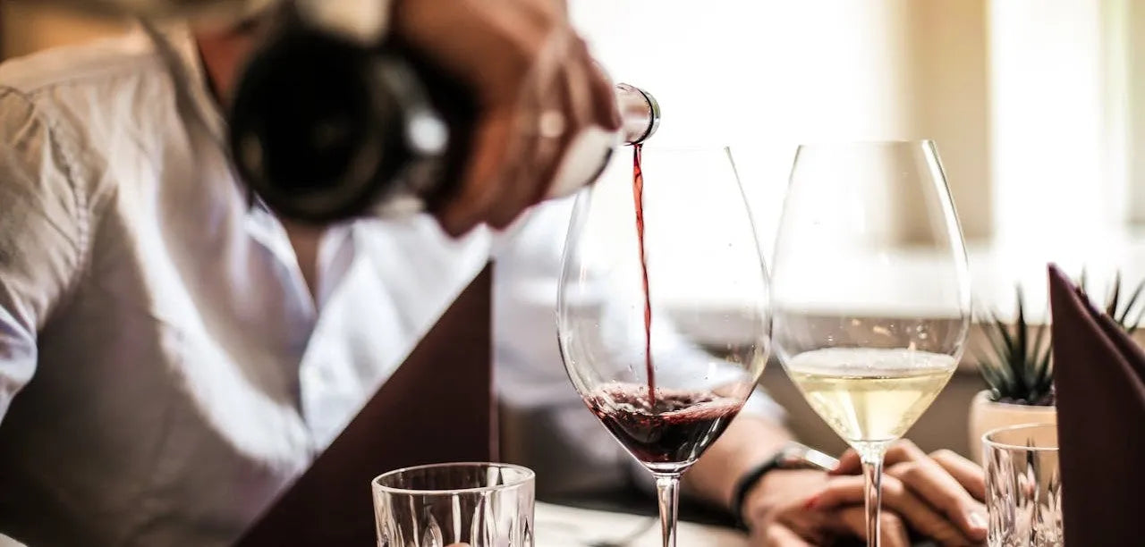 Et glas hvidvin og rødvin, som står ved siden af hinanden, imens der bliver hældt et glas rødvin op.