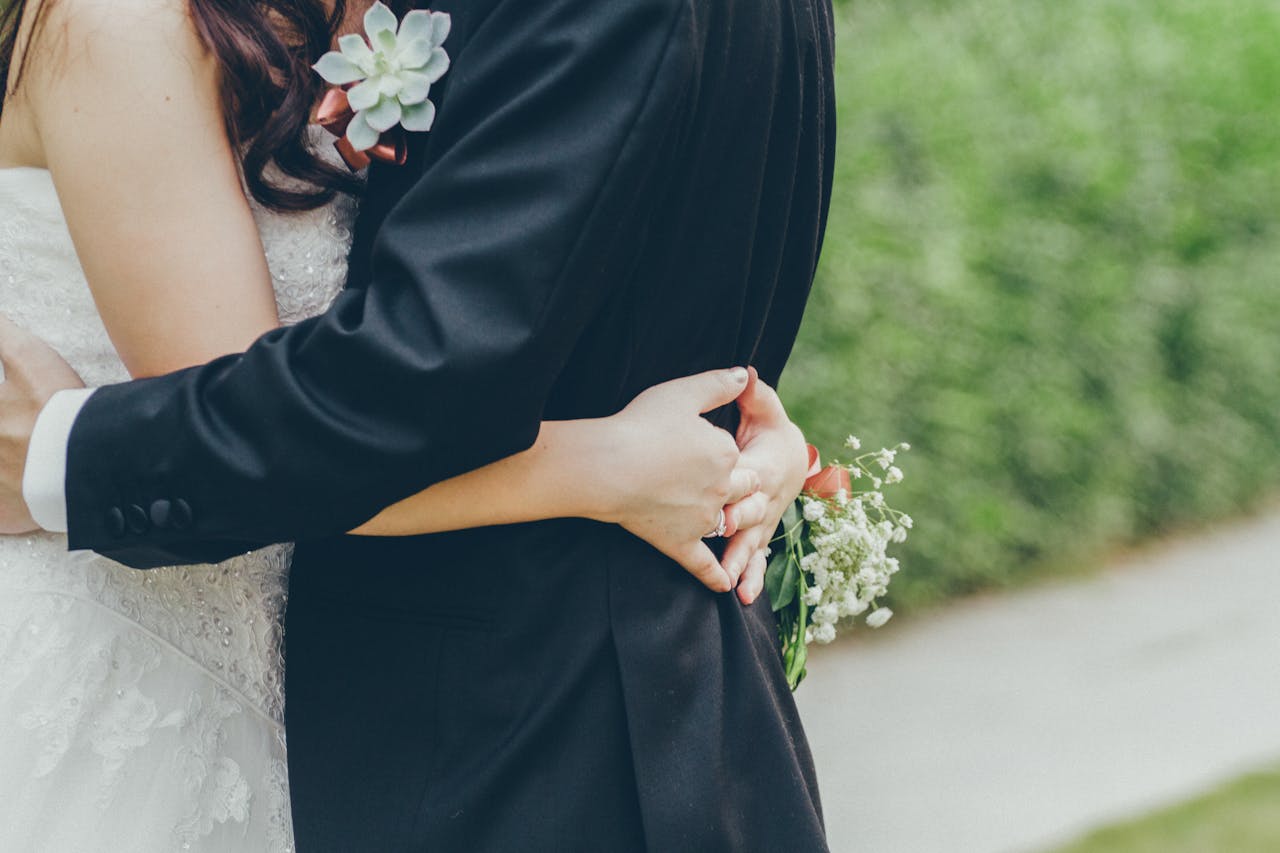 Nærbillede af et nygift par, der omfavner hinanden. Bruden iført en hvid brudekjole og brudgommen iført en sort smoking med en boutonniere.